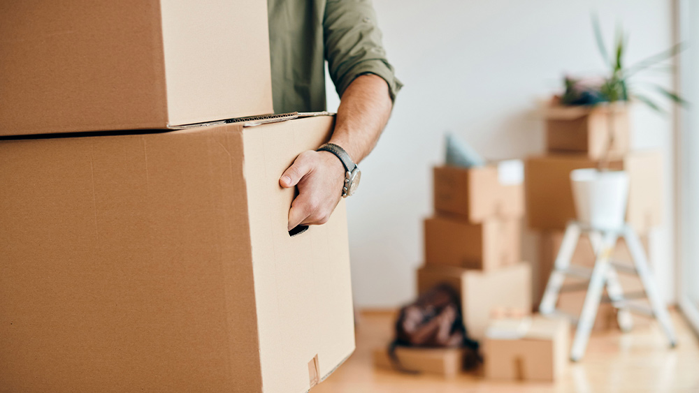 Close up of man’s hands carrying cardboard boxes with slightly blurred stacked boxes in the background